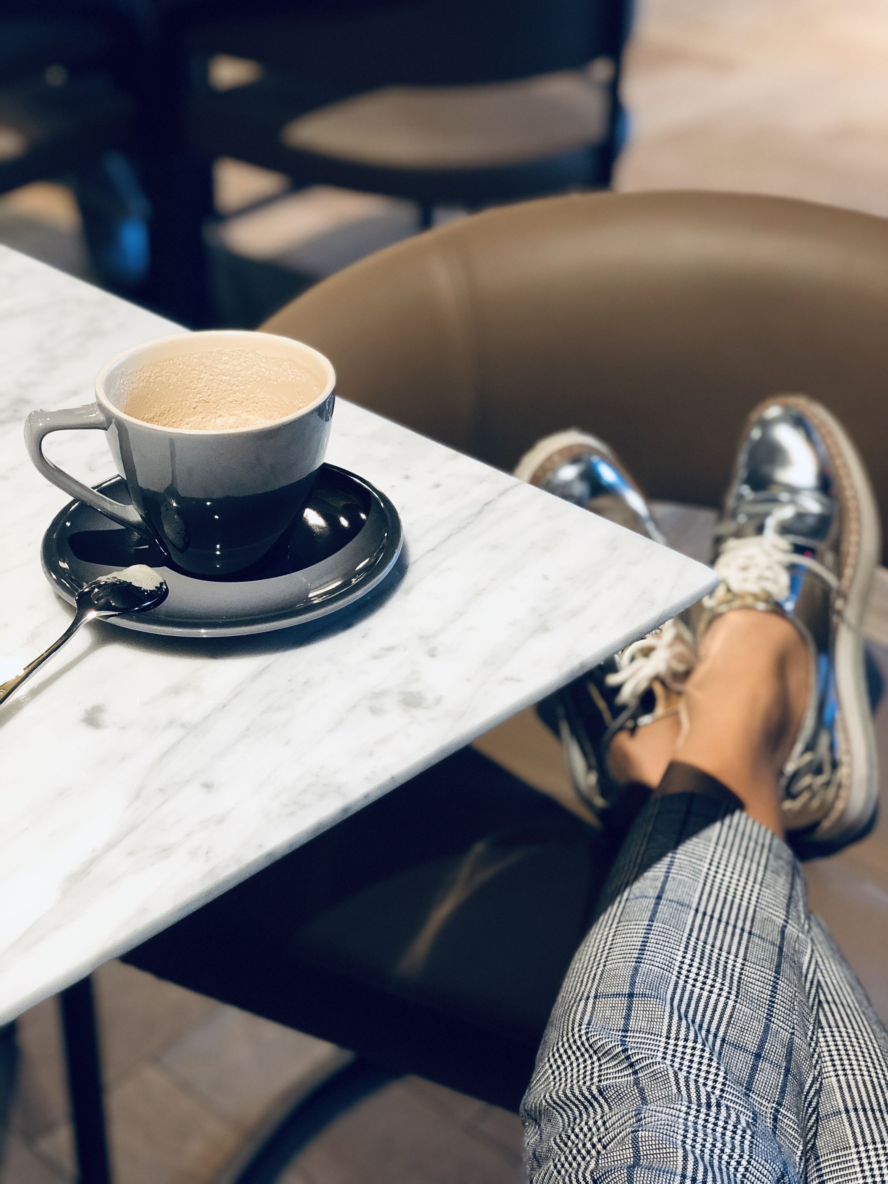 Une personne assise à une table, devant une tasse de café et une cuillère.