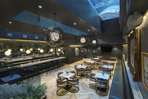 A modern restaurant with a bar area, multiple seating options, and a high ceiling with skylights.