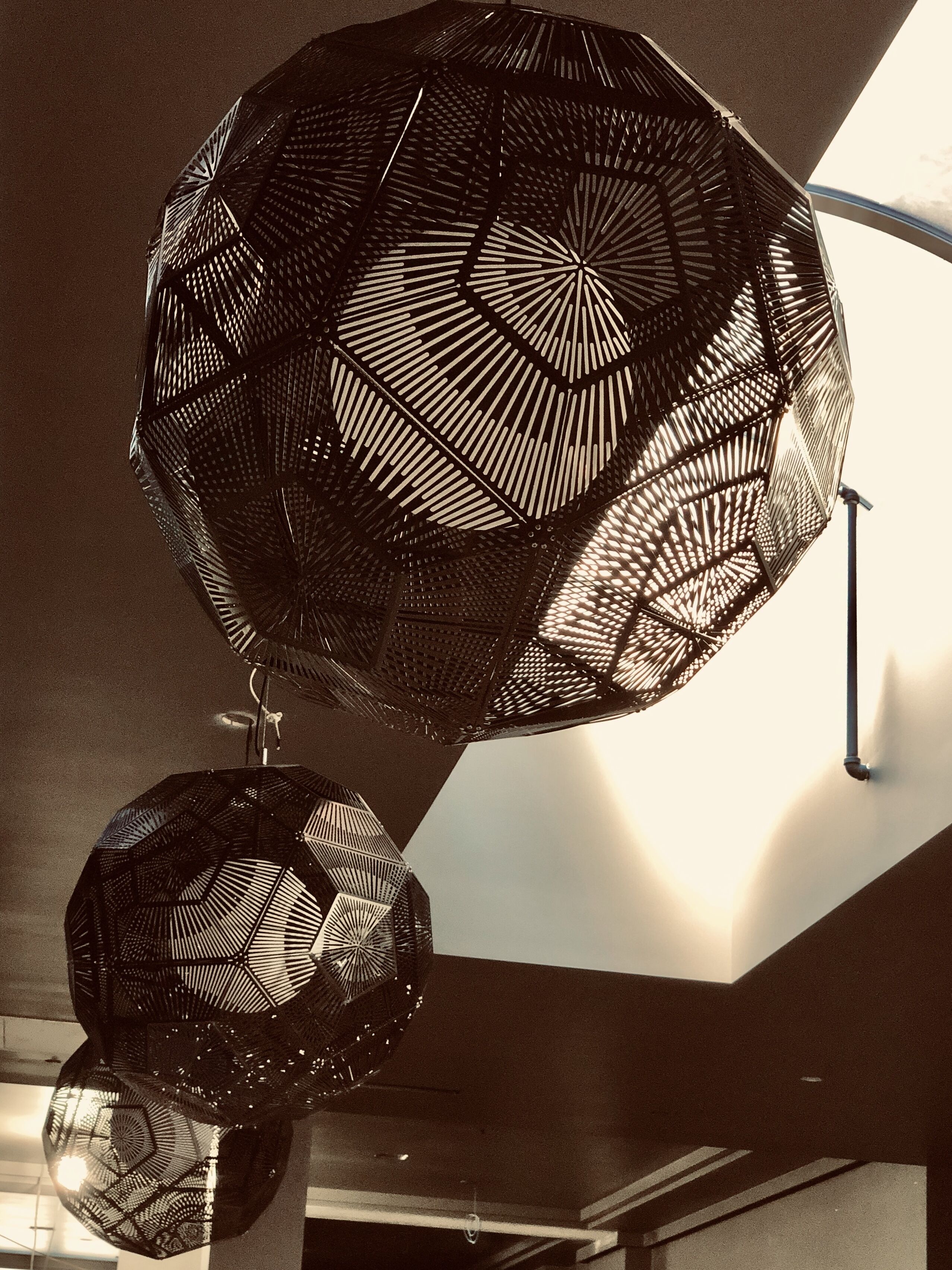 Dos lámparas grandes de estilo geométrico y metal, con diseño de panal, suspendidas del techo en un espacio interior moderno.