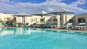 A clear blue pool with lounge chairs and umbrellas.