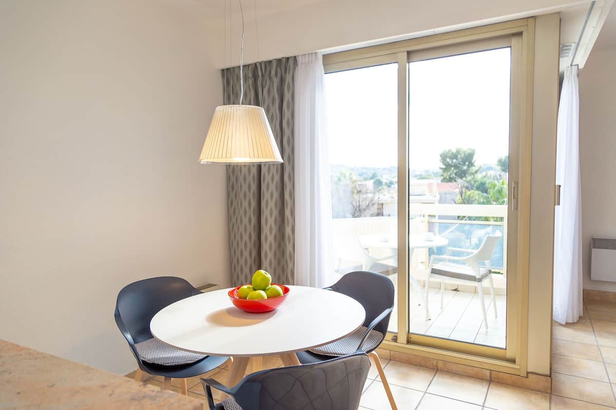 A modern dining area with a round table, two chairs, a bowl of fruit, and a large sliding glass door leading to an outdoor balcony.