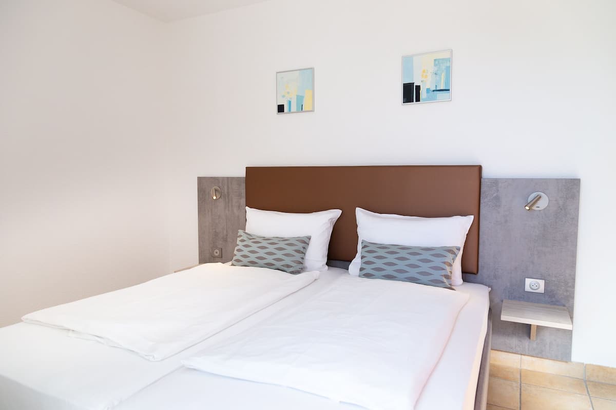 A double bed with white bedding and two pillows, a wooden headboard, and a small bedside table with a lamp.