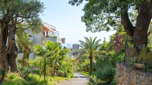 A pathway flanked by lush greenery and a stone wall, leading to a building with a red roof.