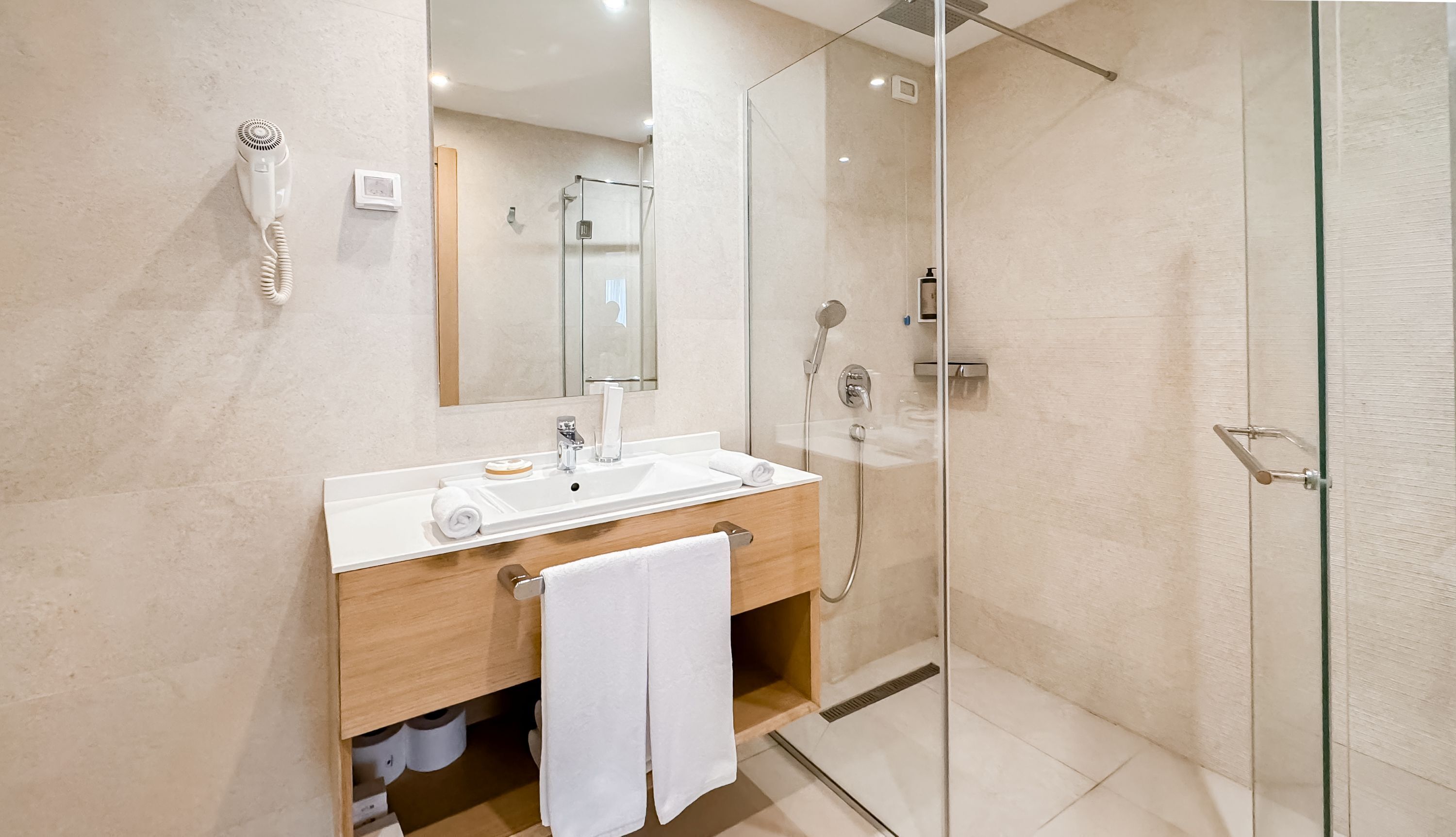 A modern bathroom with a glass-enclosed shower, a wooden vanity, a white sink, and a large mirror.