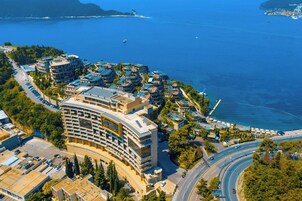 Un hotel costero con una edificación curva, estacionamiento y vista al mar.