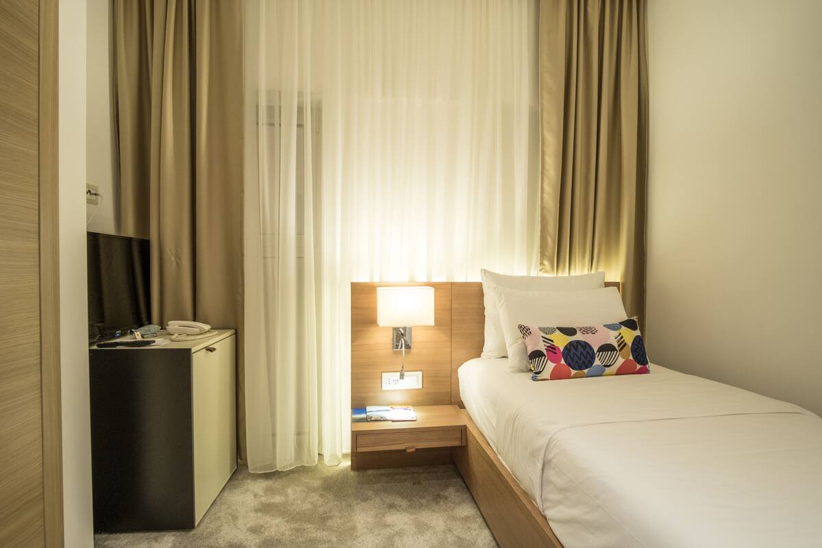 Ein Hotelzimmer mit Bett, Nachttisch, Lampe und Vorhängen.