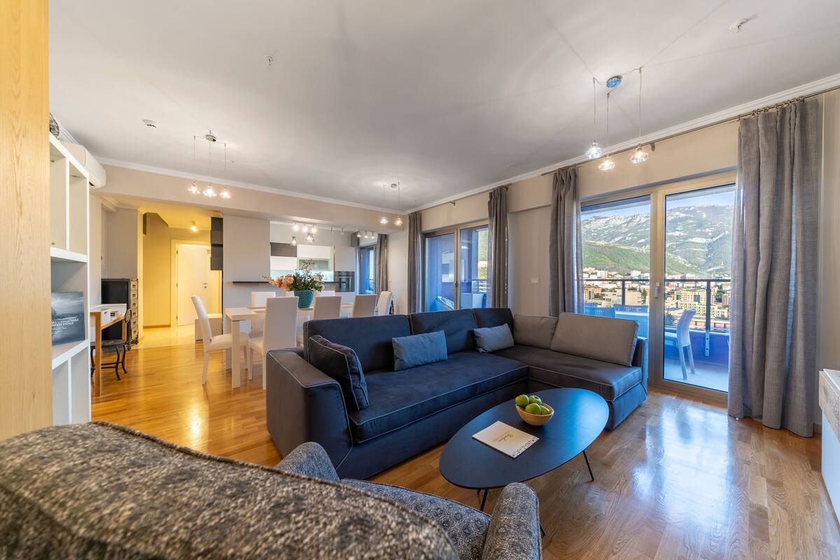 Ein modernes Wohnzimmer mit einem dunkelblauen Ecksofa, einem runden Couchtisch und einem Essbereich mit weißen Stühlen.