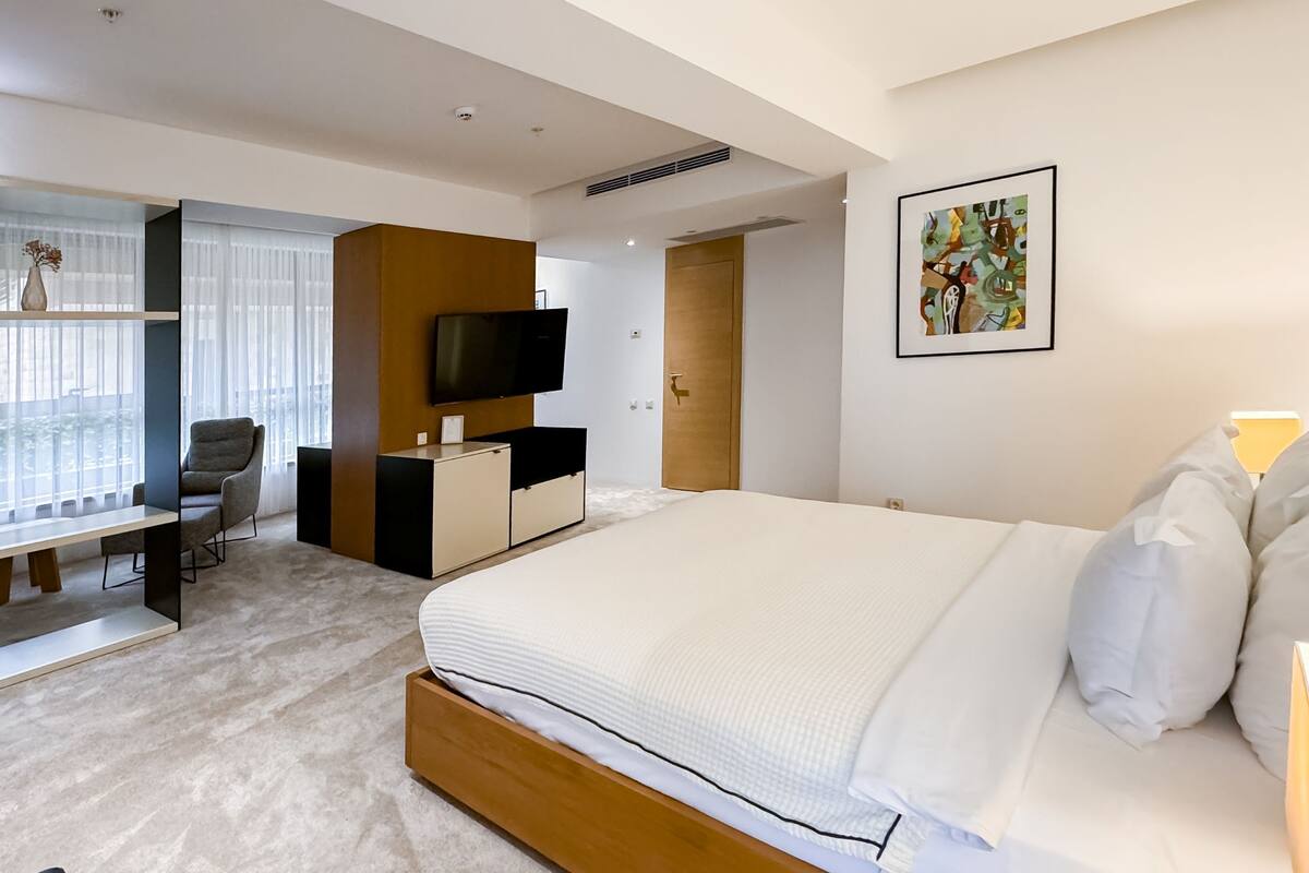 Ein modernes Hotelzimmer mit einem großen Bett, einem Schreibtisch mit Stuhl, einem Fernseher und einem Fenster mit Vorhängen.
