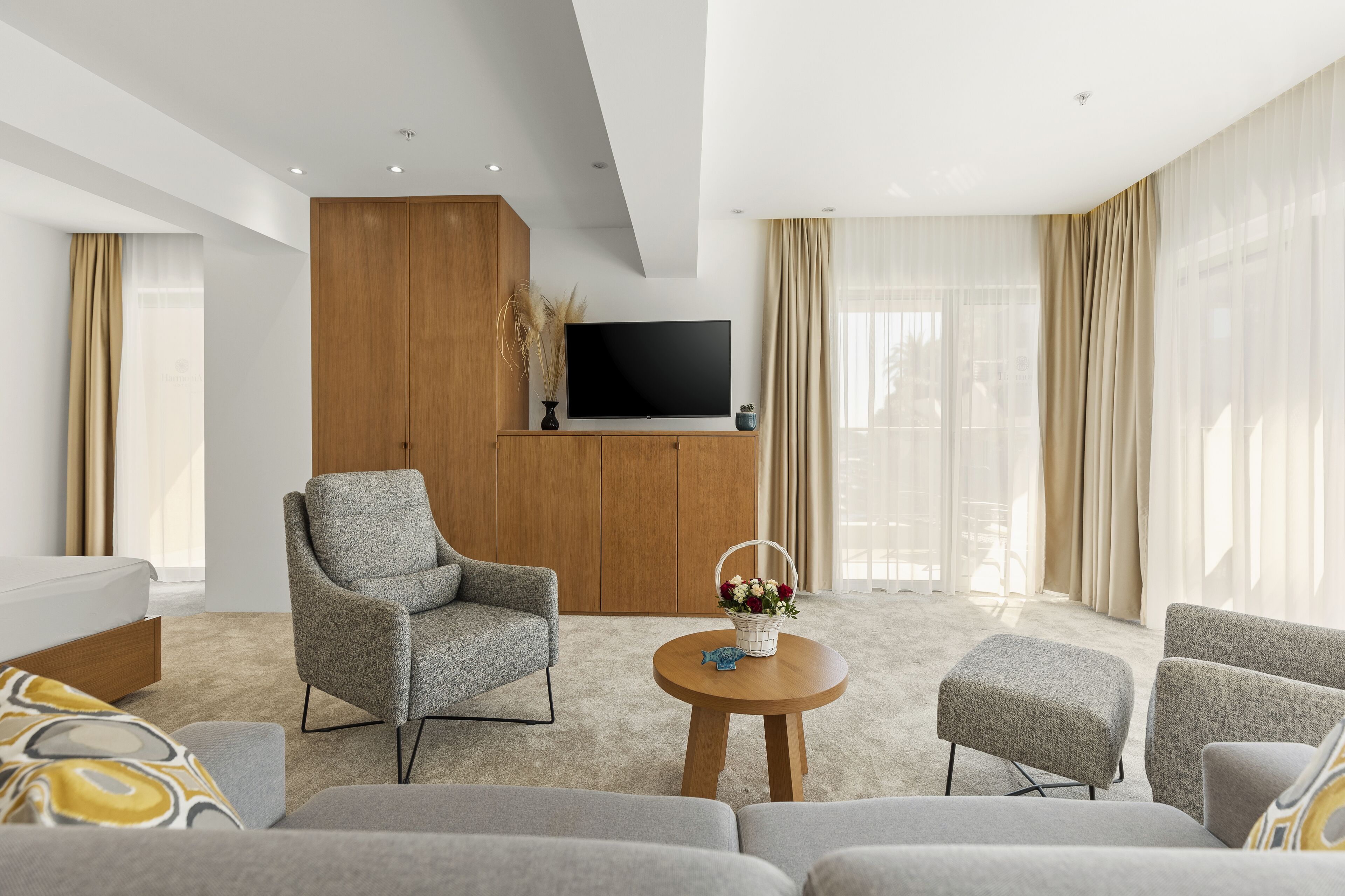Un salon moderne avec un canapé, un fauteuil, un pouf et un téléviseur posé sur un meuble en bois.