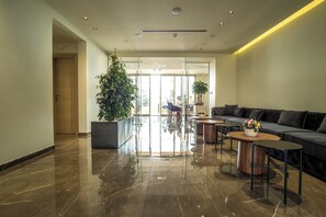 Un hall d’entrée moderne avec un sol en marbre poli, un canapé de couleur sombre et deux tables rondes ornées de compositions florales.