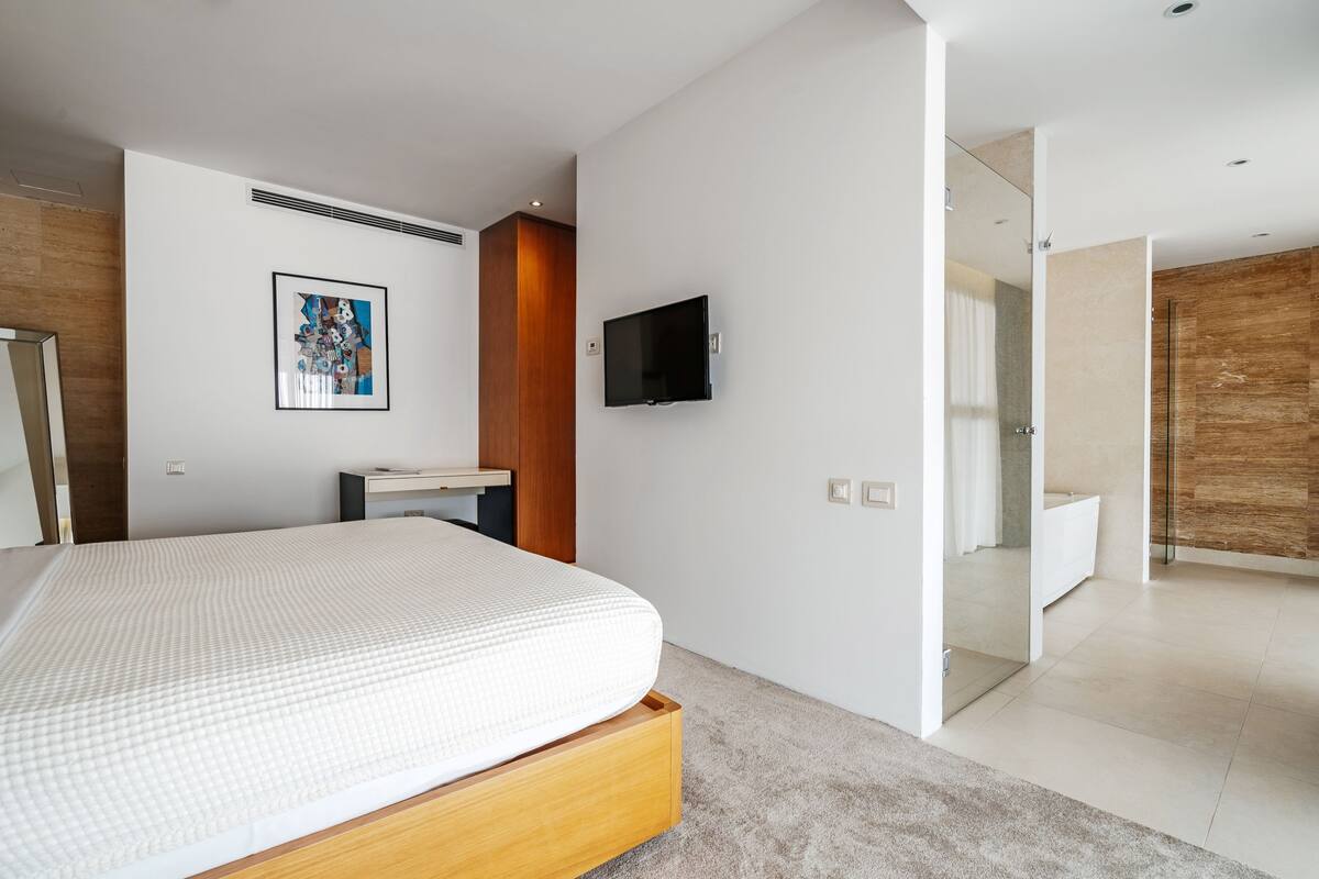 Ein modernes Schlafzimmer mit einem großen Bett, einem an der Wand montierten Fernseher und einer Wand mit Holzverkleidung.