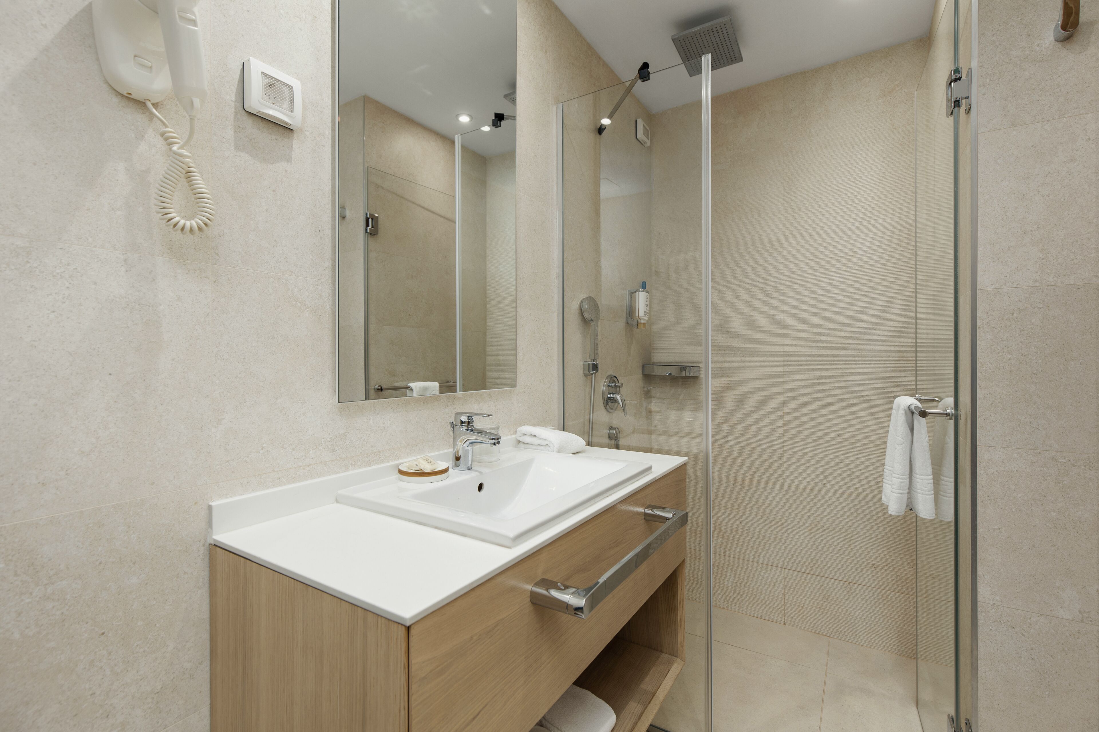 A modern bathroom with a double sink vanity, a glass shower enclosure, and a mounted hairdryer.