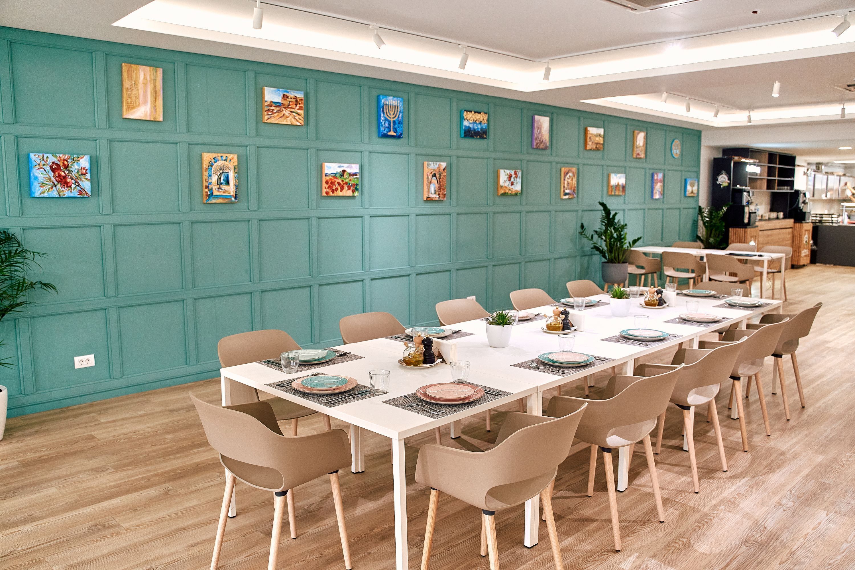 A conference room with a long table, beige chairs, teal walls, and various artworks.