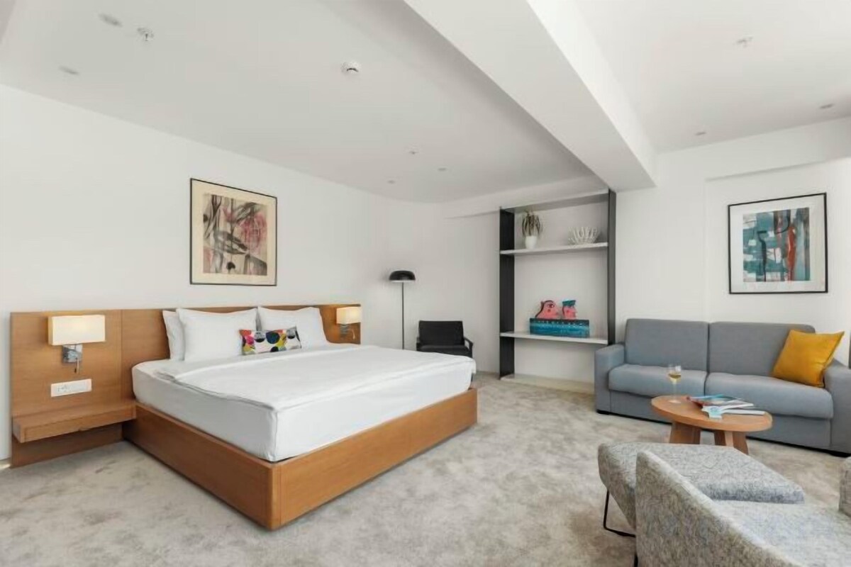 A modern hotel room with a large bed, a sofa, a chair, and a small table.