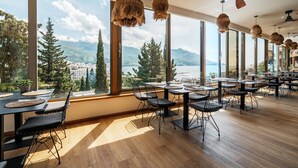 A spacious dining area with large windows offering a view of a lake and mountains. - Hotel Harmonia by Dukley (Budva)