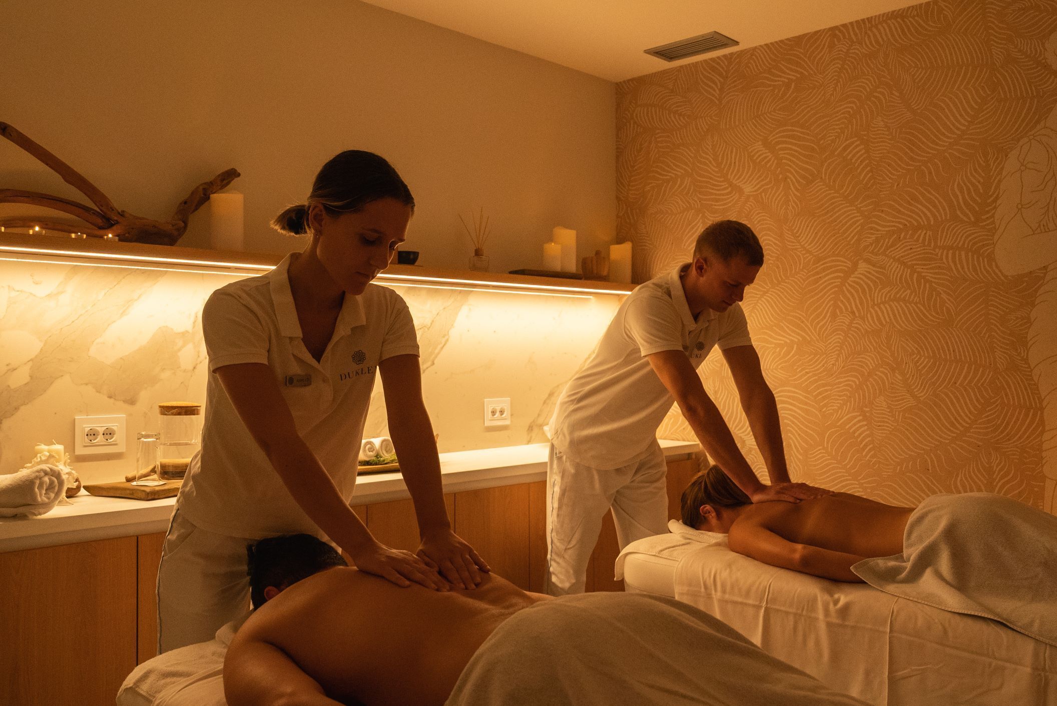A massage therapy room with a wooden counter, a massage table, and a patterned wall.