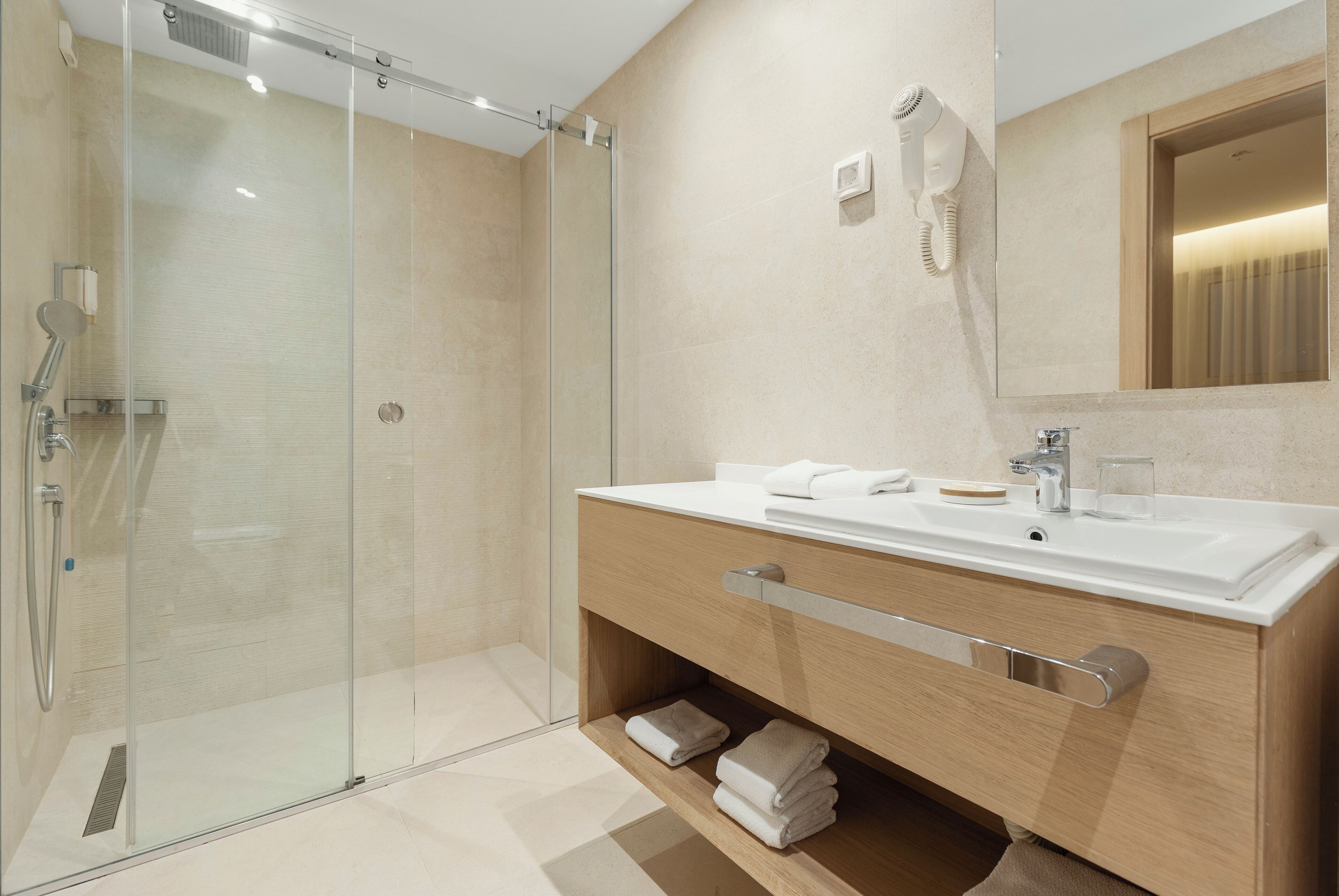 A modern bathroom with a glass-enclosed shower, a wooden vanity with a sink, and a hairdryer mounted on the wall.