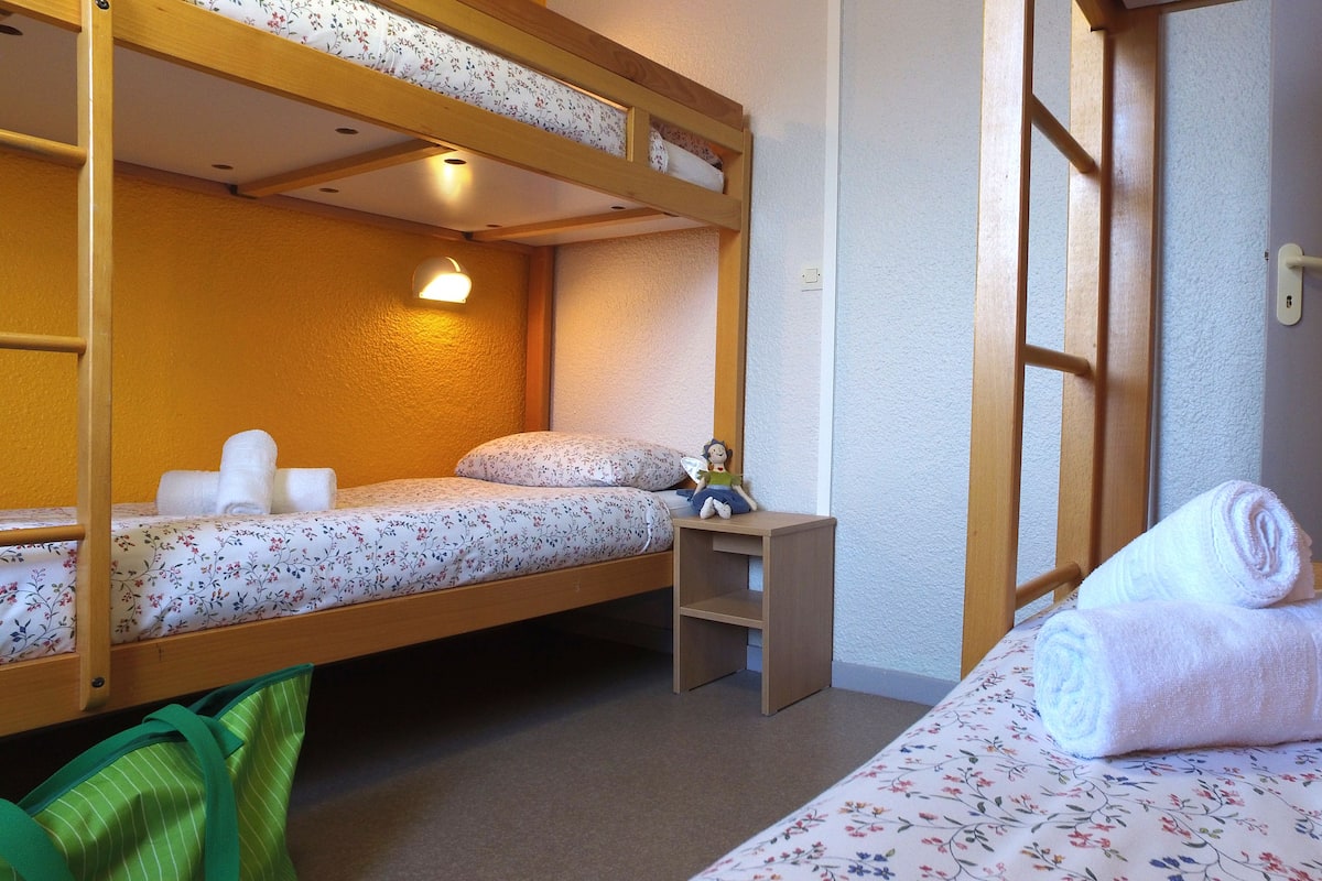 A dormitory room with two bunk beds, a small desk, and a rolled-up towel on the lower bunk.