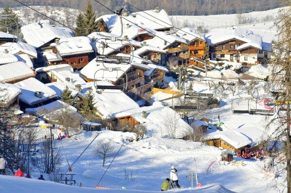 A snow-covered village with wooden buildings, ski lifts, and a ski slope.