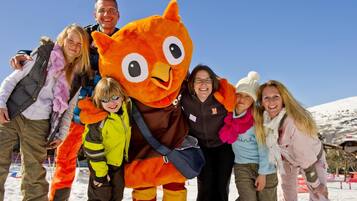 Eine Gruppe von Menschen posiert mit einer großen, orangefarbenen Maskotte in einer verschneiten Winterlandschaft.
