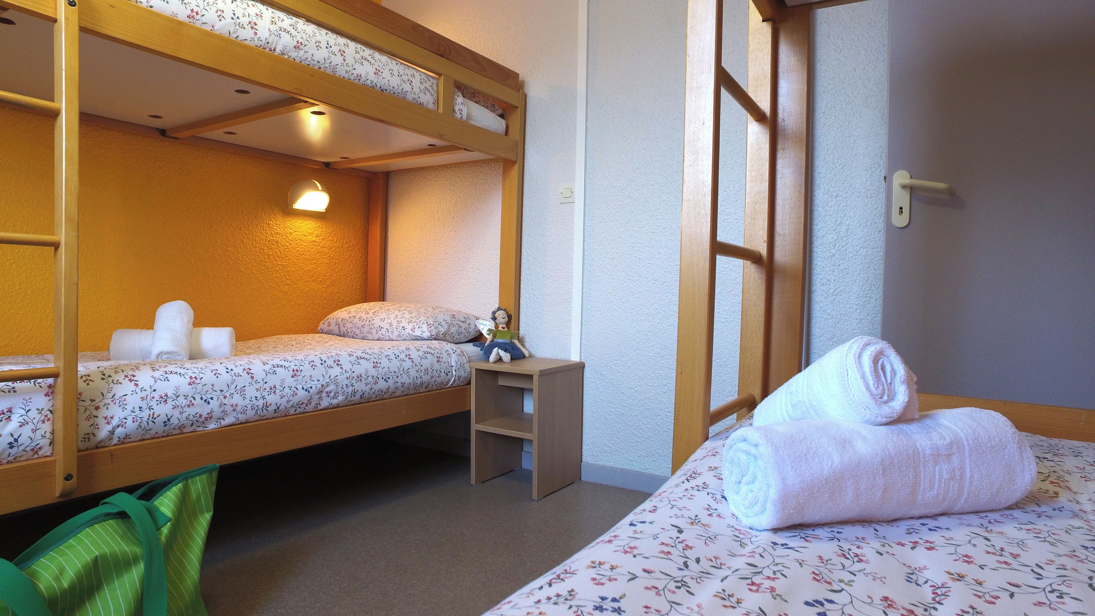 A bunk bed room with a small desk, a wall-mounted shelf, and a rolled towel on the bed.