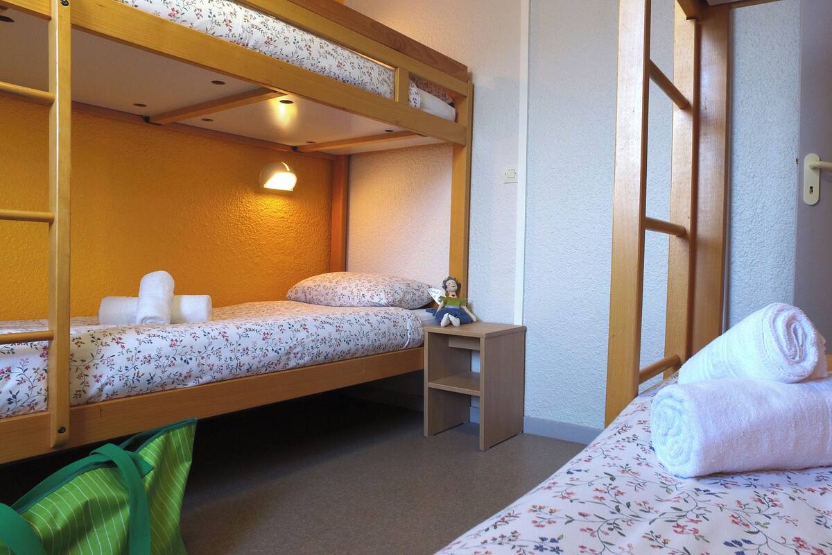 A dormitory room with two bunk beds, a small desk, and a rolled-up towel on the lower bunk.