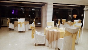 A banquet hall with round tables and chairs, each with a white tablecloth and a yellow sashed chair. - Hotel Bauji Palace (Udaipur)