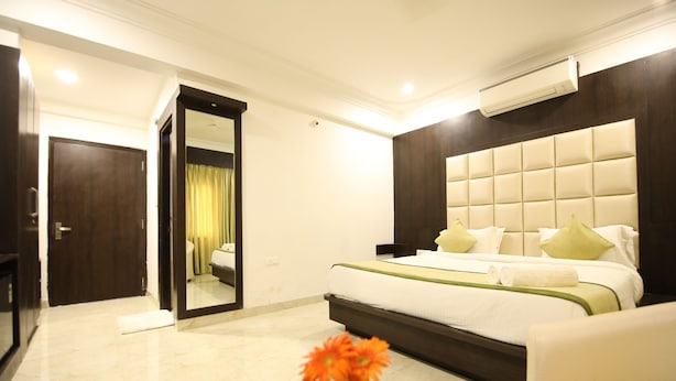 A hotel room with a large bed, a mirror, a glass coffee table with a vase of flowers, and a dark wooden headboard. - Hotel Bauji Palace (Udaipur)