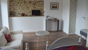 A bedroom with a stone wall, a bed, a small round table, a sofa, and a television on a shelf. - Mont Voyageur (Sains)