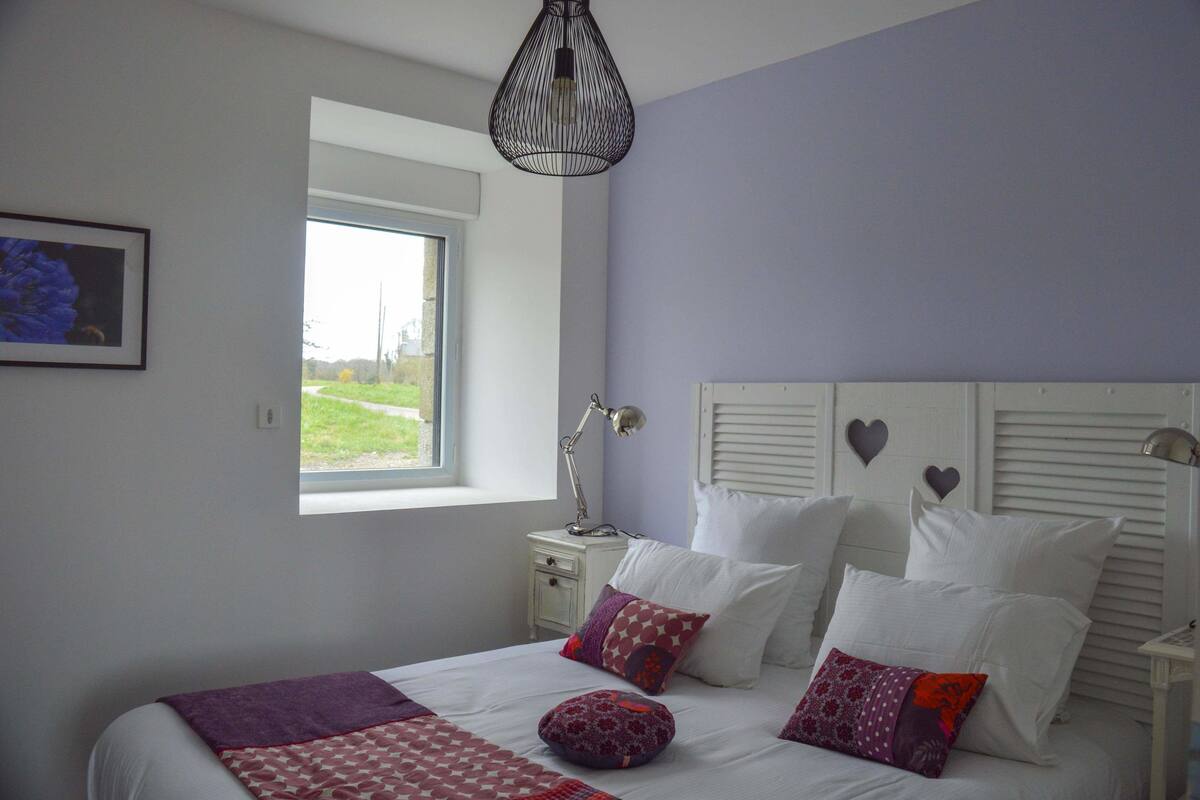 A bedroom with a bed, pillows, a nightstand, a lamp, and a window.