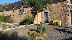A stone building with a sloped roof, a small outdoor seating area with a bench, and a gravel driveway. - Mont Voyageur (Sains)
