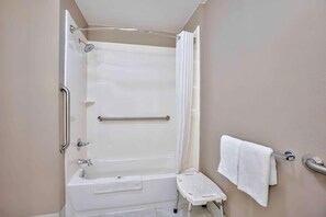 Un baño con bañera, ducha, pasamanos, barra de apoyo, perchero y un pequeño taburete.