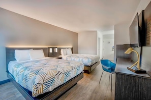 Une chambre d’hôtel avec deux lits, un bureau, une chaise et un téléviseur.