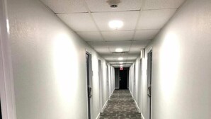 Un pasillo largo y estrecho con alfombra estampada, paredes blancas y puertas a ambos lados.