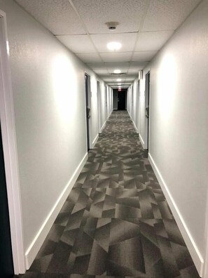 A long, narrow hallway with patterned carpet, white walls, and doors on both sides.