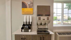 Una estación de café con una cafetera, tazas y un cartel en la pared.