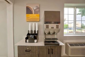 A coffee station with a coffee machine, cups, and a poster on a wall.