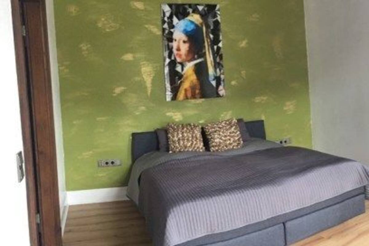 A bedroom with a bed, a chair, a window with curtains, and a painting on the wall.