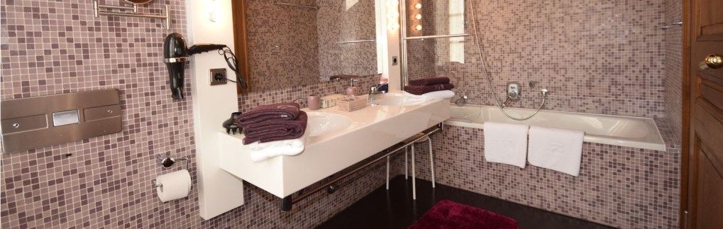 Een badkamer met een grote spiegel, twee wasbakken, een haardroger en een bad.