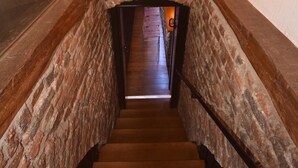 Una escalera de madera con paredes de piedra y vista a una habitación inferior.