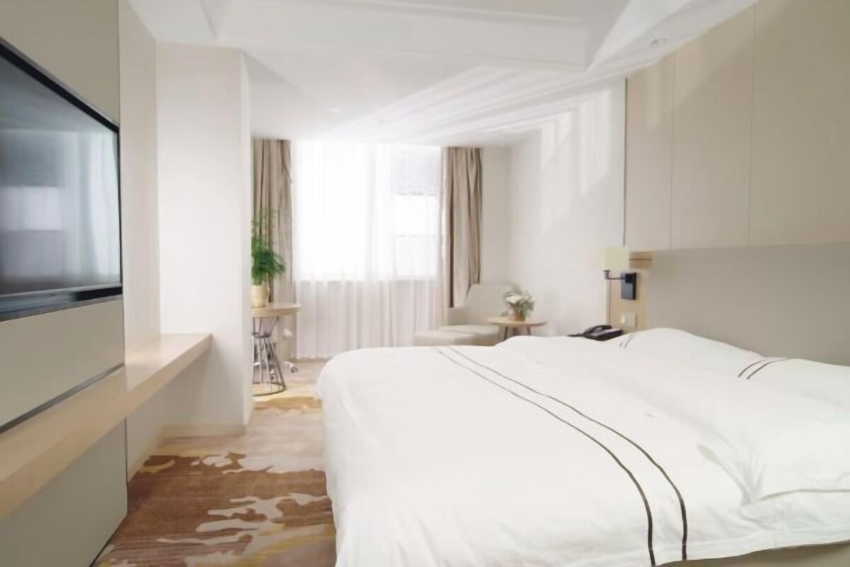 Una habitación de hotel moderna con una cama grande, televisión, escritorio y ventana con cortinas.