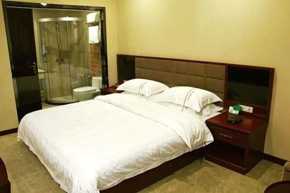 Una habitación de hotel con cama, mesita de noche, televisor y ducha con mampara de vidrio.