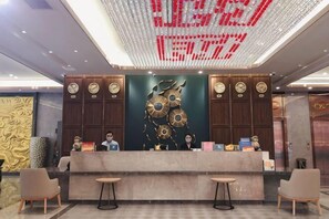 Un mostrador de recepción de hotel con un reloj digital, un elemento decorativo grande en la pared y un área de espera con tres sillas.