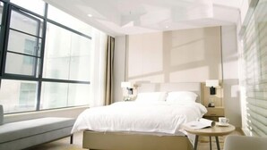 A hotel room with a large window, a bed, a bedside table with a lamp, and a chair. - Yu Long Jin Hotel (Ezhou)