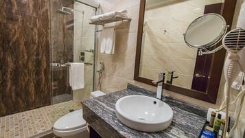 Een badkamer met een douchecabine van glas, een wastafel met een marmeren blad, een toilet en een grote spiegel.