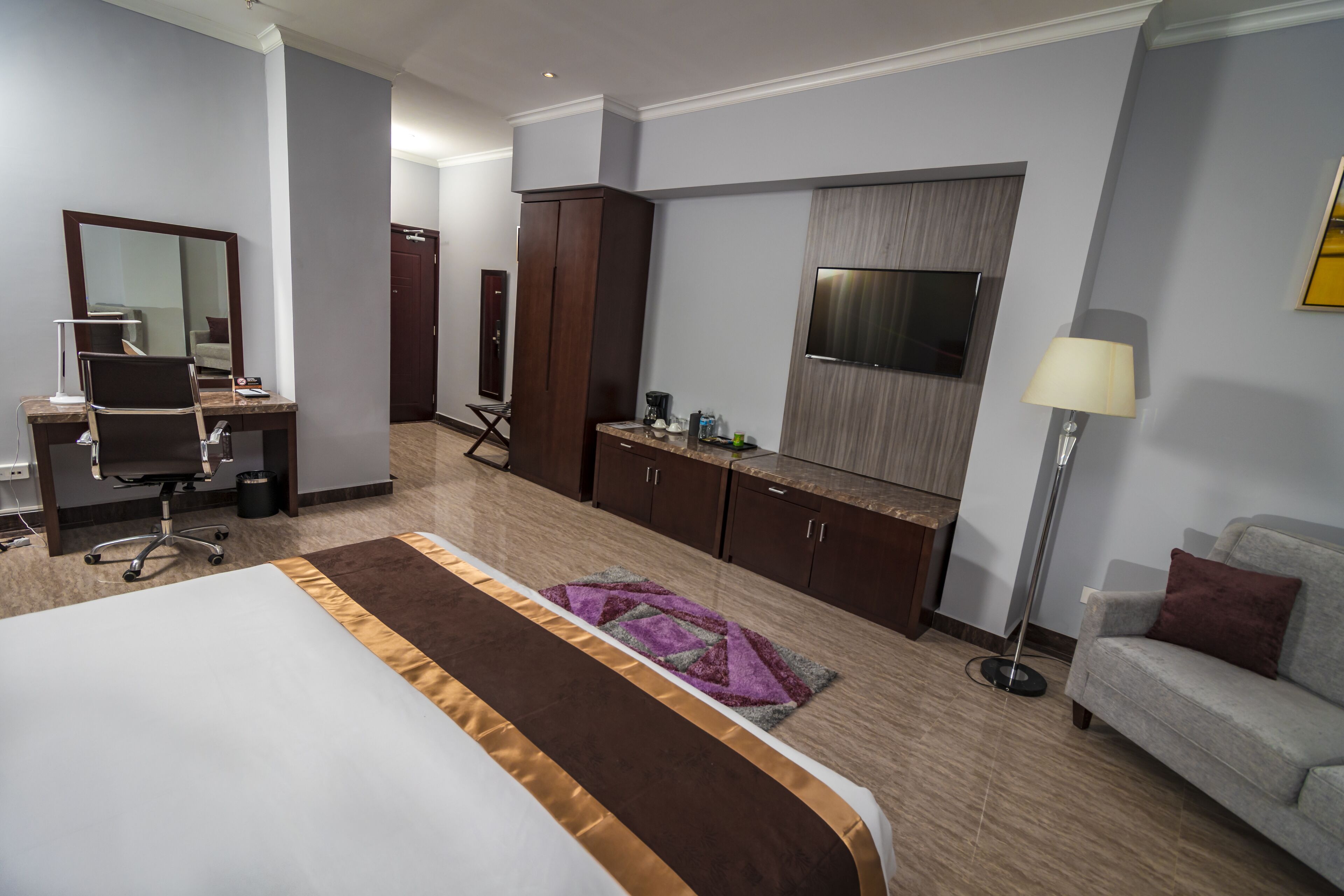 Una habitación de hotel con cama, escritorio con silla, armario, televisor, sofá y lámpara de pie.