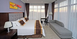 A hotel room with a large bed, a sofa, a desk, and a chair.