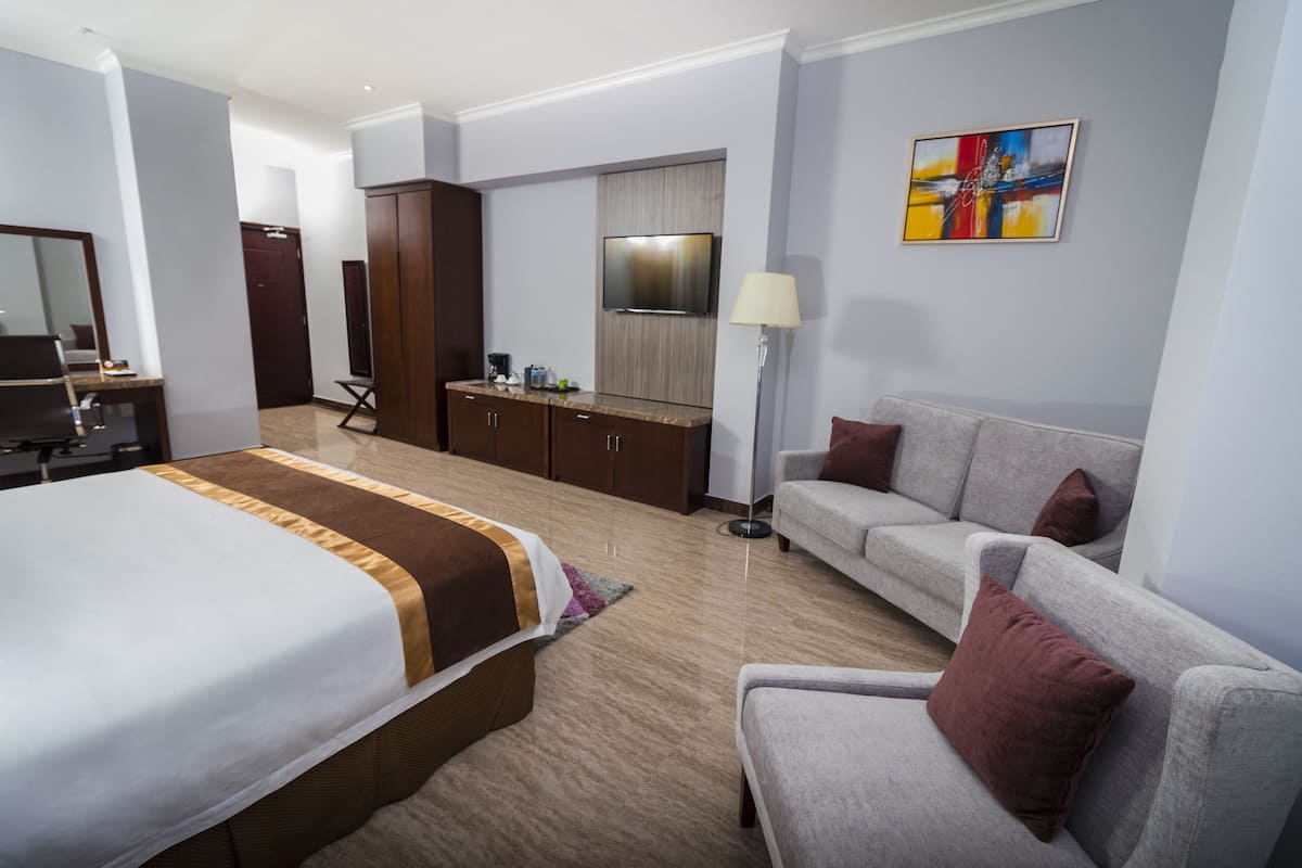 A hotel room with a large bed, a sofa, a desk, a TV, and a painting on the wall.