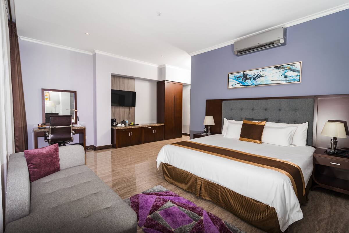 A hotel room with a large bed, a desk with a chair, a television, and a wardrobe.