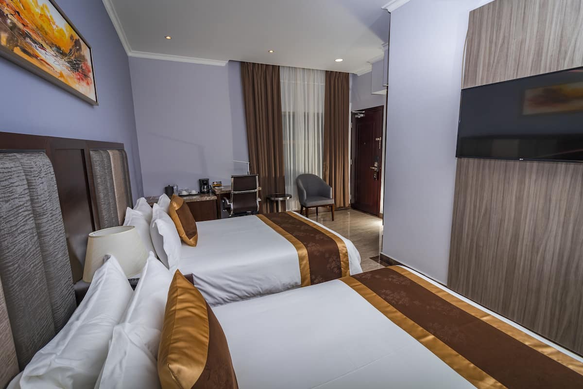 A hotel room with two beds, a desk, a chair, a TV, and a painting on the wall.